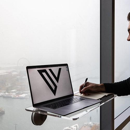 A photo of a clear DeskView desk suctioned to a large window with a view of the water.